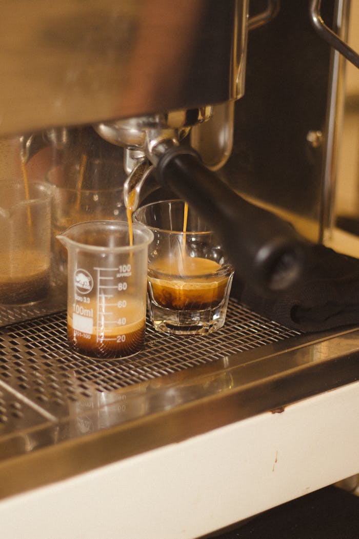 Close-up of espresso brewing into glass and beaker, showcasing coffee extraction process.